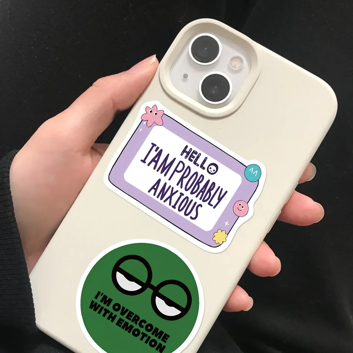A hand holds a phone displaying humorous stickers about anxiety and overcoming emotions.