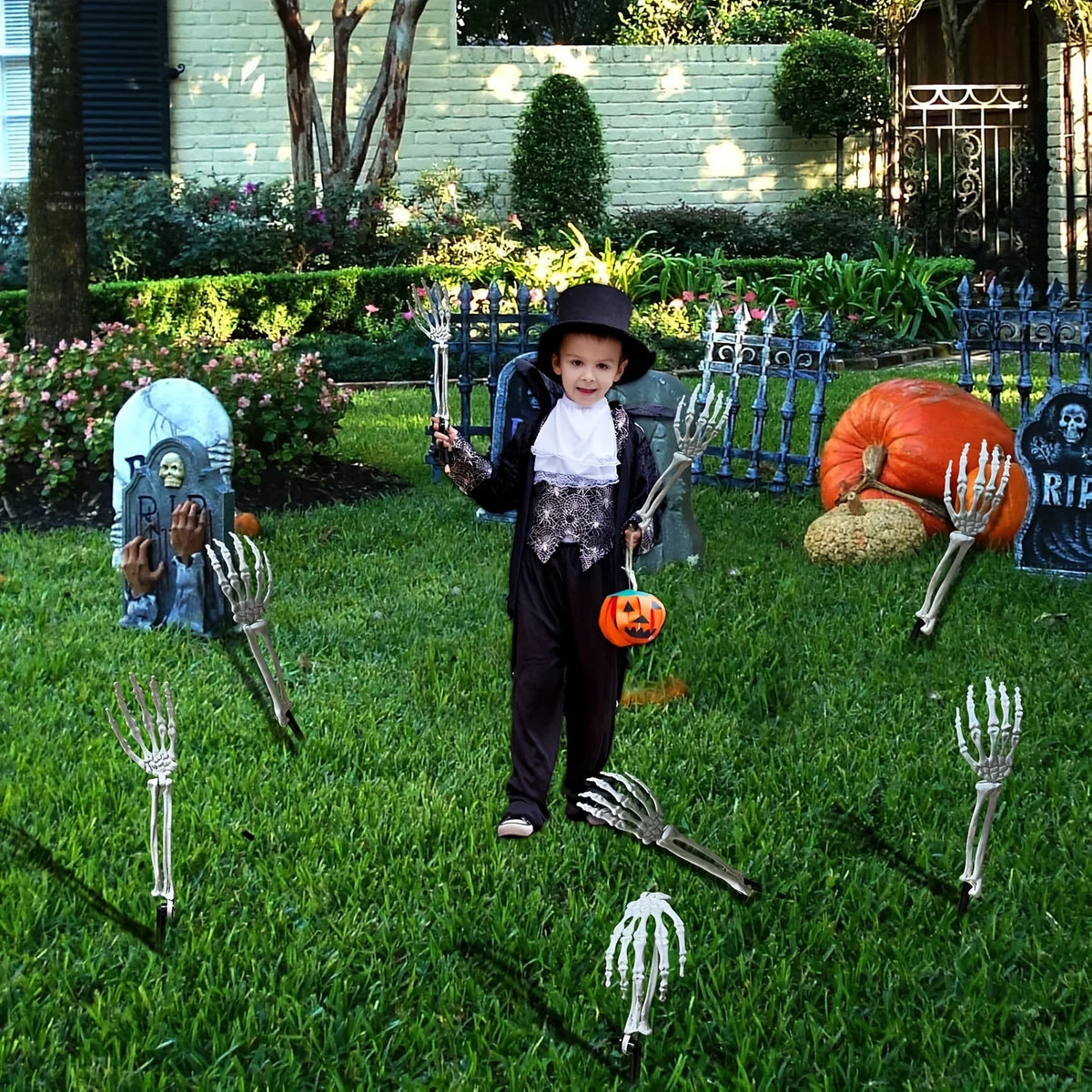 A child dressed in black stands in a garden with various Halloween skeleton bone stakes and an orange pumpkin.