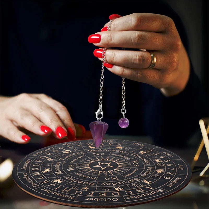 A hand holds a silver chain pendant with a purple gemstone over a wooden divination board.