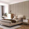 A bedroom featuring a bed with light beige linens against a wall covered in vertical wood grain panels.