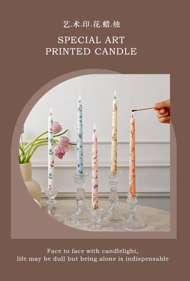 A collection of tall, slender printed candles in pink and green floral patterns displayed on a light surface.
