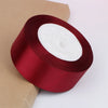 A roll of deep red satin ribbon with a white center core, shown against a light brown paper background.