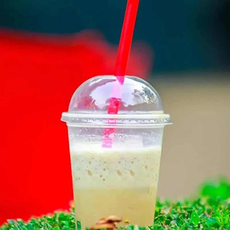 A clear plastic cup filled with a light-colored drink and a red straw, resting on green moss.