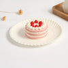 A stack of pink and white layered cake on a white paper plate with red berries, set against a white background.