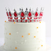 Gâteau à étages blanc décoré d'une couronne en métal de cristal scintillant et de petites perles oranges comestibles.