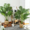 Artificial areca palm tree in a woven pot displayed on a wooden surface.
