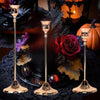 A set of three matte gold taper candle holders displayed on a dark surface with autumn foliage and a pumpkin.