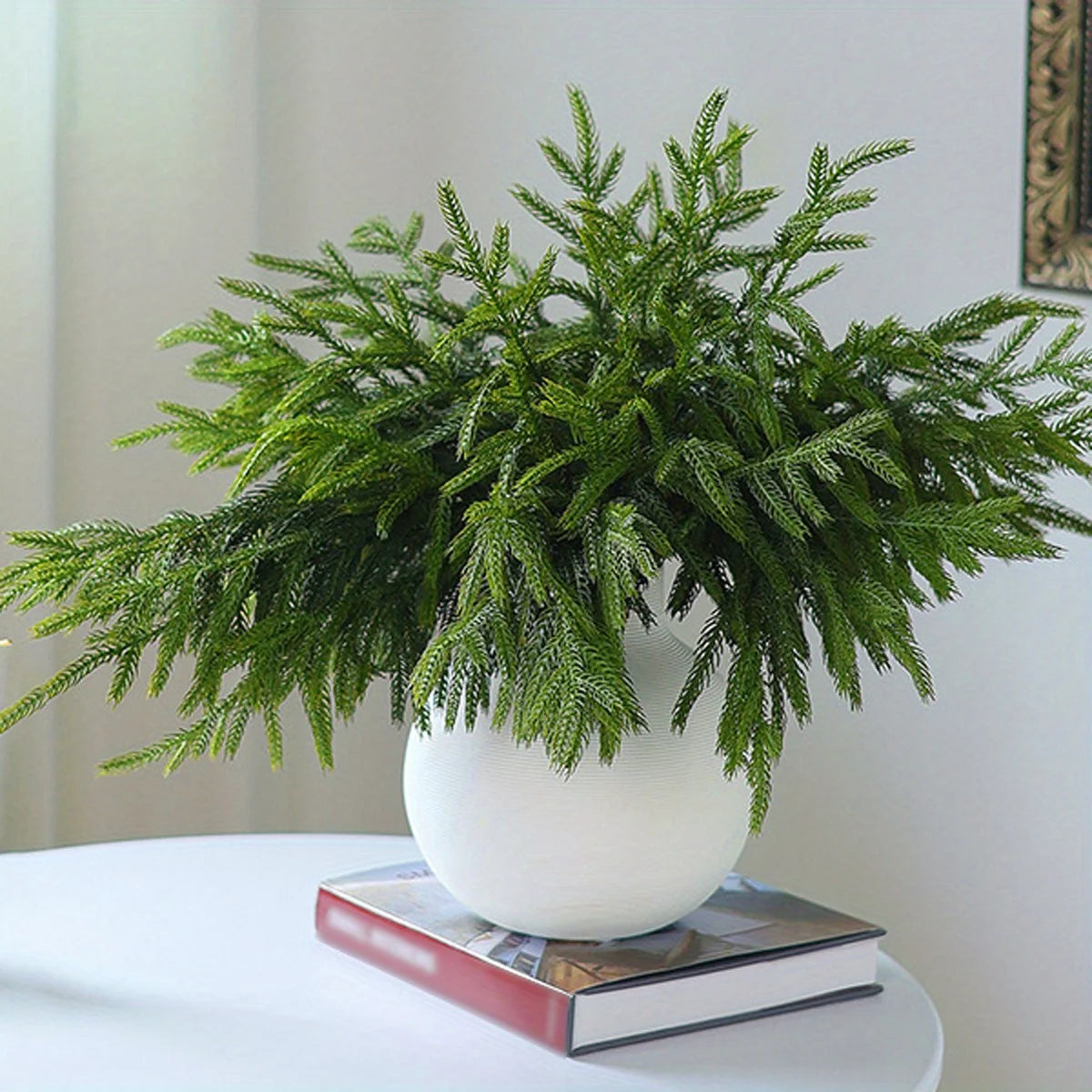 Lifelike artificial pine branches in a white ceramic vase on a table.