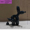 A black sculpture of a dog in a squatting position made from a balloon, displayed on a light surface.