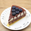 A slice of dark chocolate tart with a glossy ganache on a white plate.