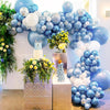 Arche florale décorée de ballons bleus et blancs et de verdure, avec un ensemble de ballons rose métallique et or rose.