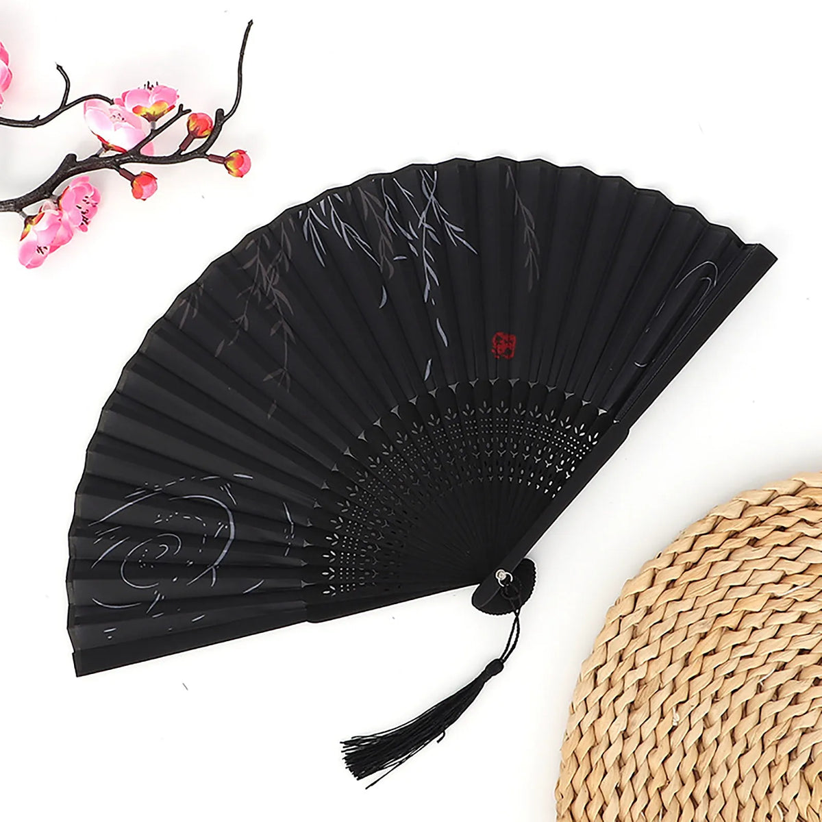 Black vintage bamboo folding fan with subtle gray patterns and a woven straw mat in the background