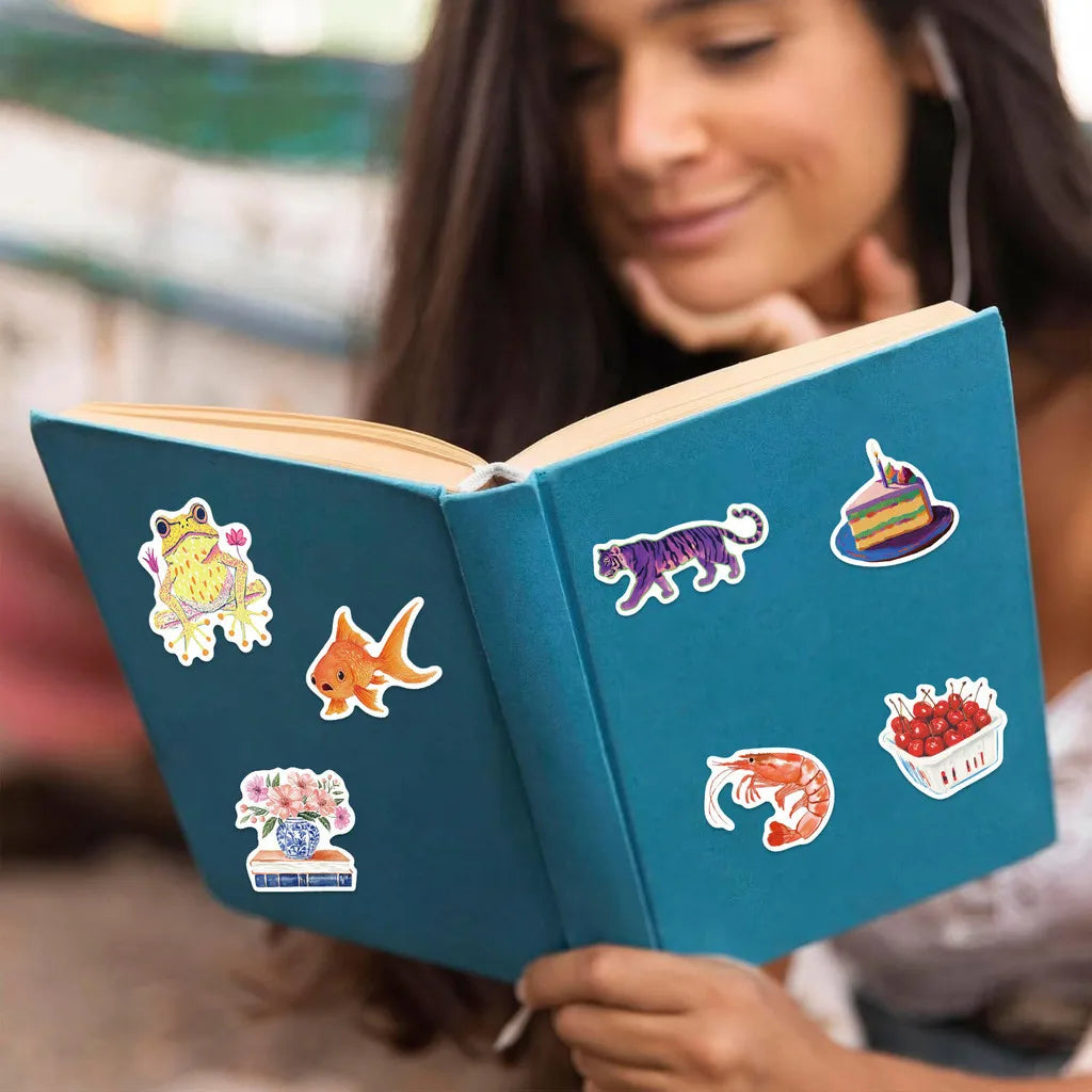 A close-up of a teal sticker book filled with colorful graffiti stickers, held by a woman.