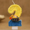 A birthday cake candle shaped like the number 9, decorated with yellow glitter and featuring a small construction excavator f