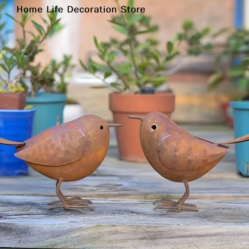 Two rustic metal bird sculptures in brown tones standing on weathered wood.