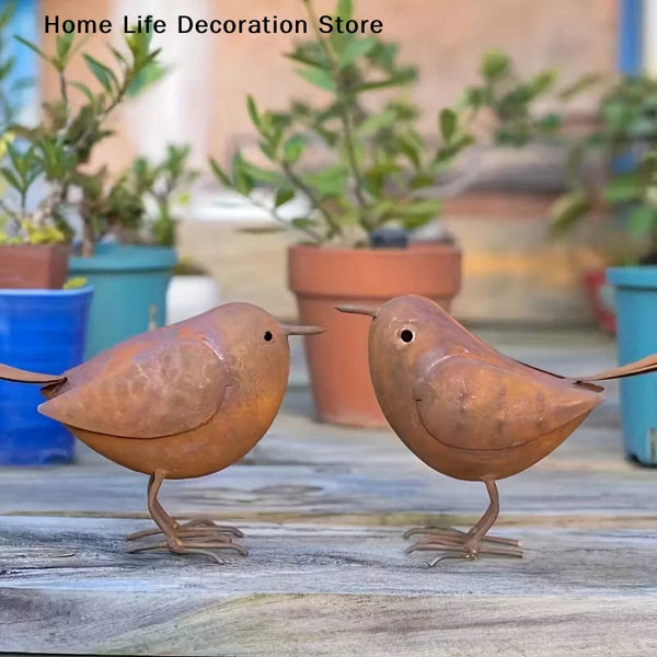 Two rustic metal bird sculptures in brown tones standing on weathered wood.