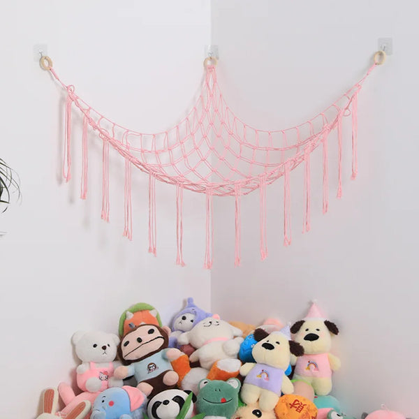 Pink cotton hammock toy for stuffed animals and plushies hanging on a white wall