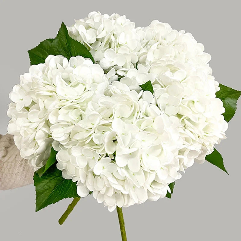 A cluster of white artificial hydrangea flowers with green leaves.