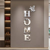 Silver acrylic wall stickers shaped like a butterfly and the word HOME mounted on a light gray wall.