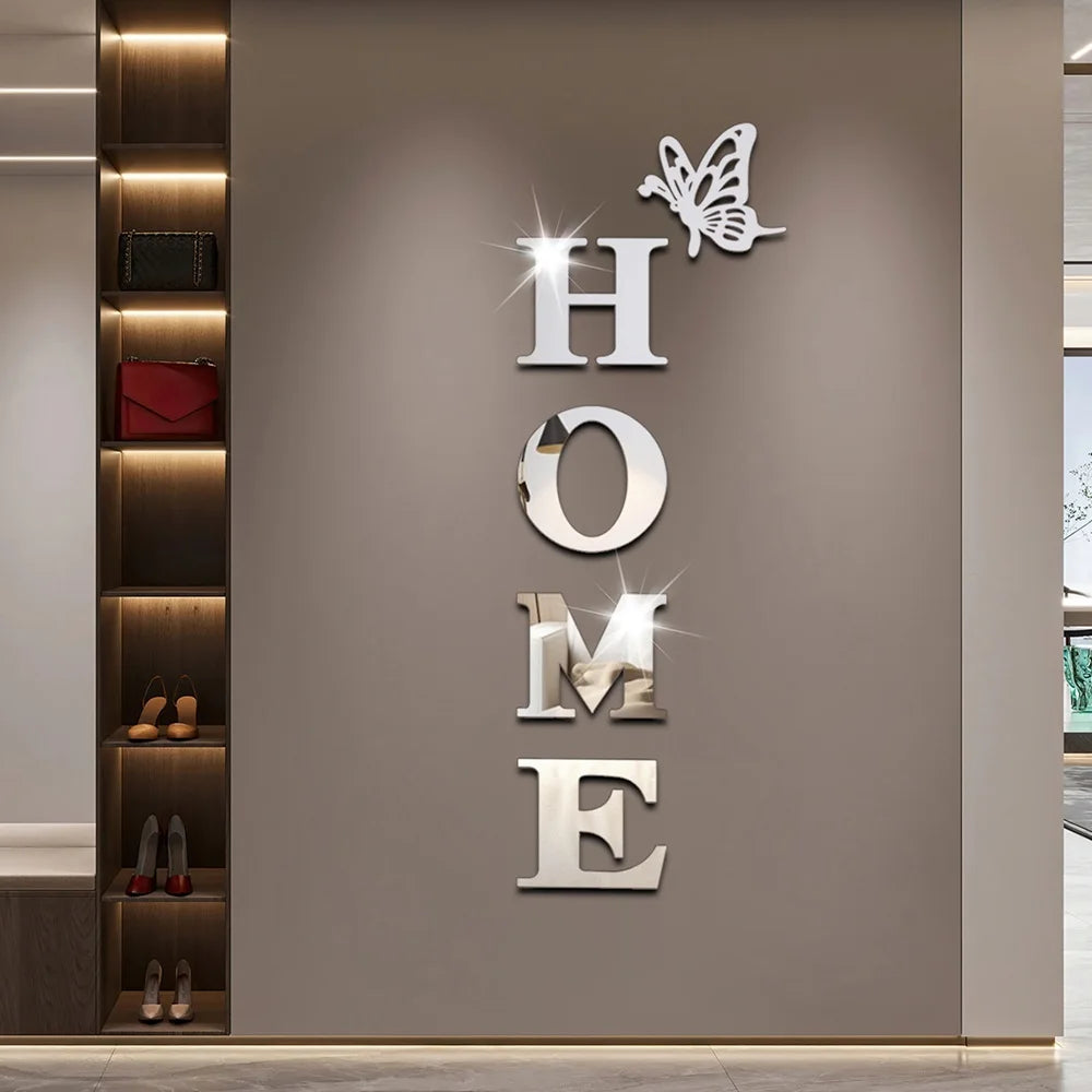 Silver acrylic wall stickers shaped like a butterfly and the word HOME mounted on a light gray wall.