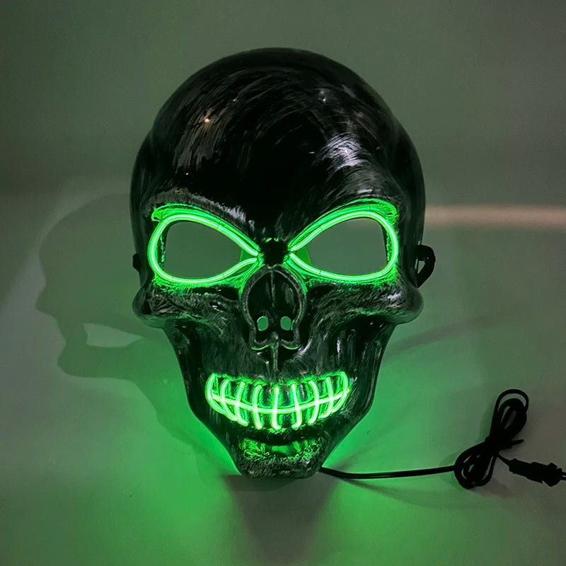 A realistic latex skull mask with glowing green eyes and teeth, displayed against a light green background.