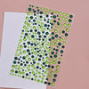 A sheet of clear adhesive featuring small green and dark green glitter gems for facial tattoos.