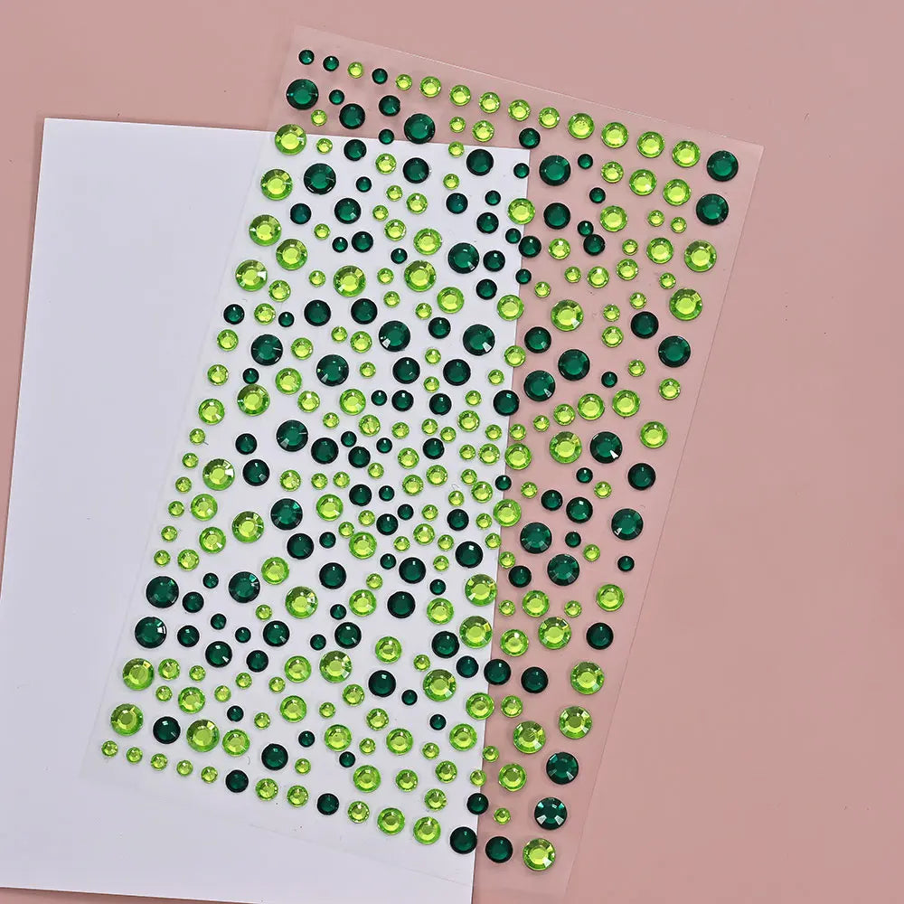 A sheet of clear adhesive featuring small green and dark green glitter gems for facial tattoos.