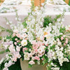 Un bouquet de fleurs artificielles blanches et roses dans un pot beige sur de l'herbe verte.