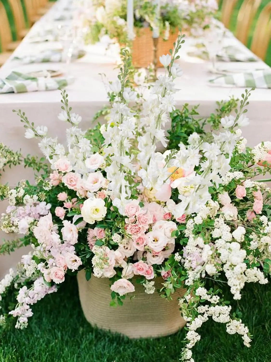 Un bouquet de fleurs artificielles blanches et roses dans un pot beige sur de l'herbe verte.