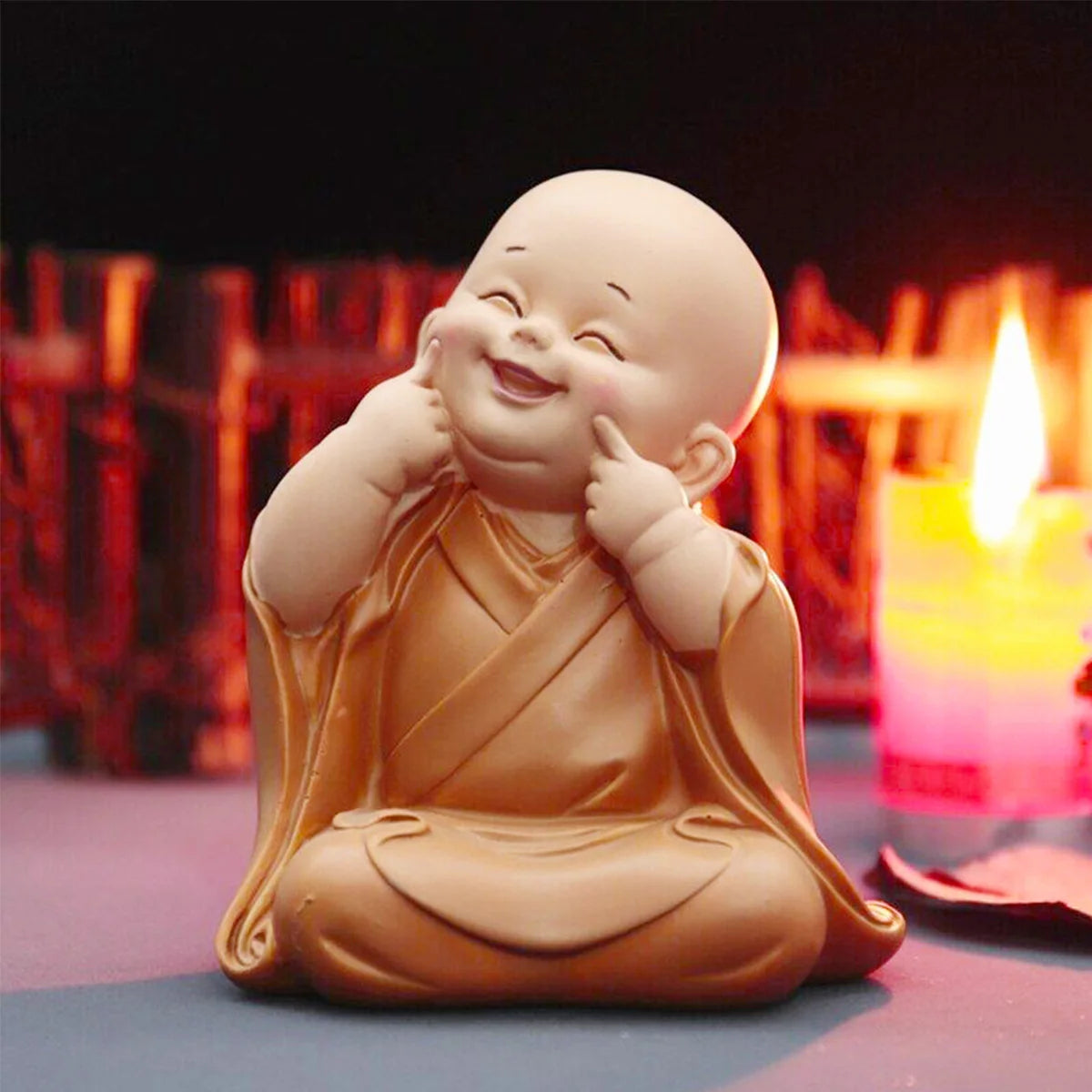 A small, smiling resin figurine of a monk in orange robes sitting in a meditative pose.