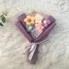 A bouquet of handcrafted crochet flowers in yellow, white, and purple nestled in a purple paper wrap.