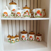 A collection of handcrafted miniature ceramic mushroom tableware for dollhouses displayed on a white shelf.