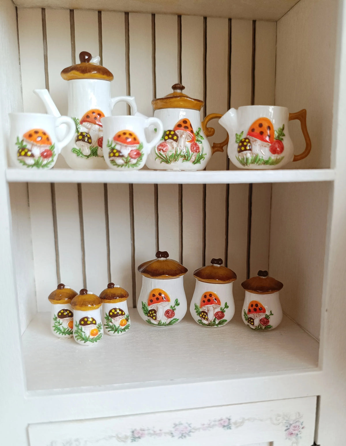 A collection of handcrafted miniature ceramic mushroom tableware for dollhouses displayed on a white shelf.
