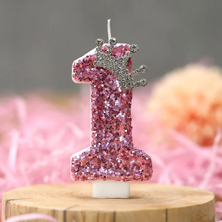 A pink glitter birthday number candle shaped like the number one with a silver crown topper
