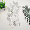A collection of twelve silver glitter butterfly wall stickers arranged on a white surface next to a potted green plant.