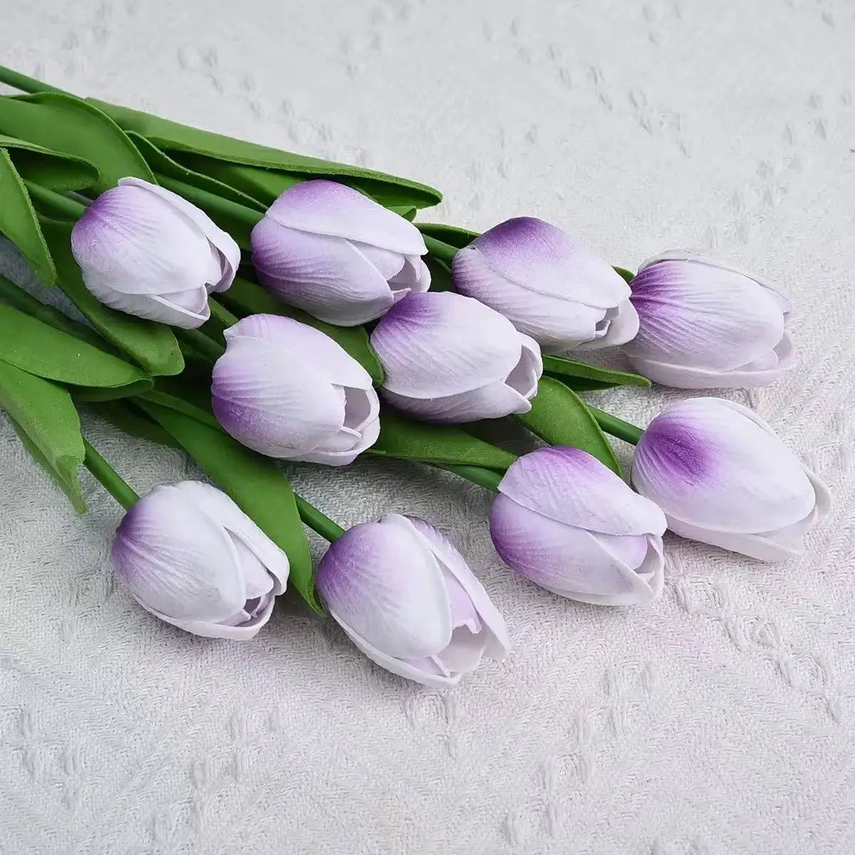A bouquet of realistic artificial tulips in shades of lavender and white on green stems.