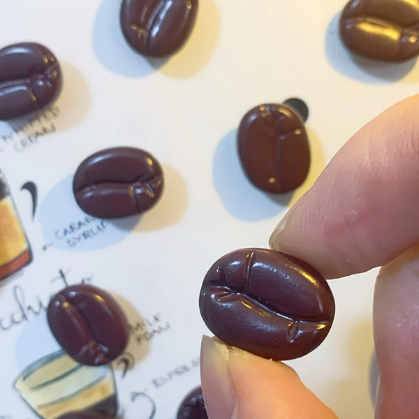 A close-up shot of several dark roasted coffee beans used as fridge magnets, held by a finger.