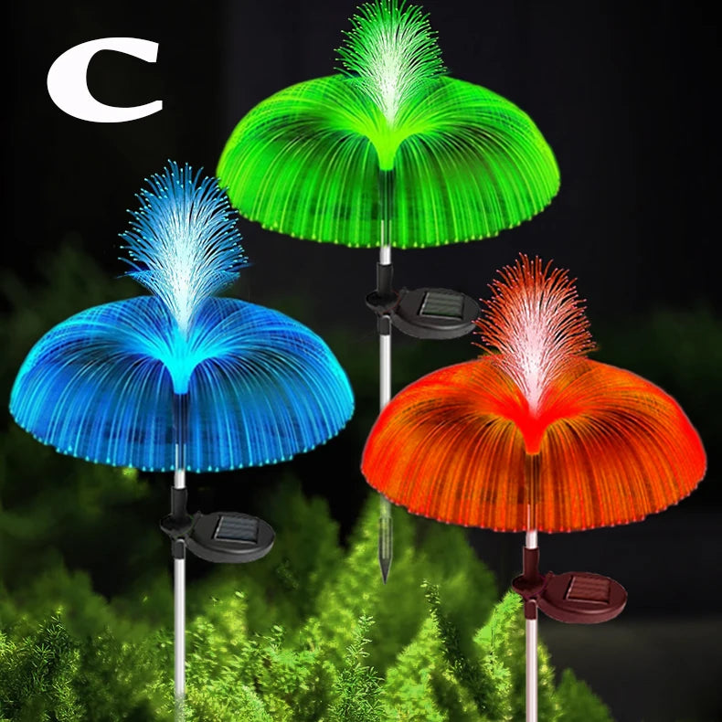 Three solar jellyfish garden lights in green, blue, and orange illuminating a green foliage background.
