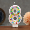 A white candle shaped like the number 8 decorated with colorful glitter candy beads for a birthday.
