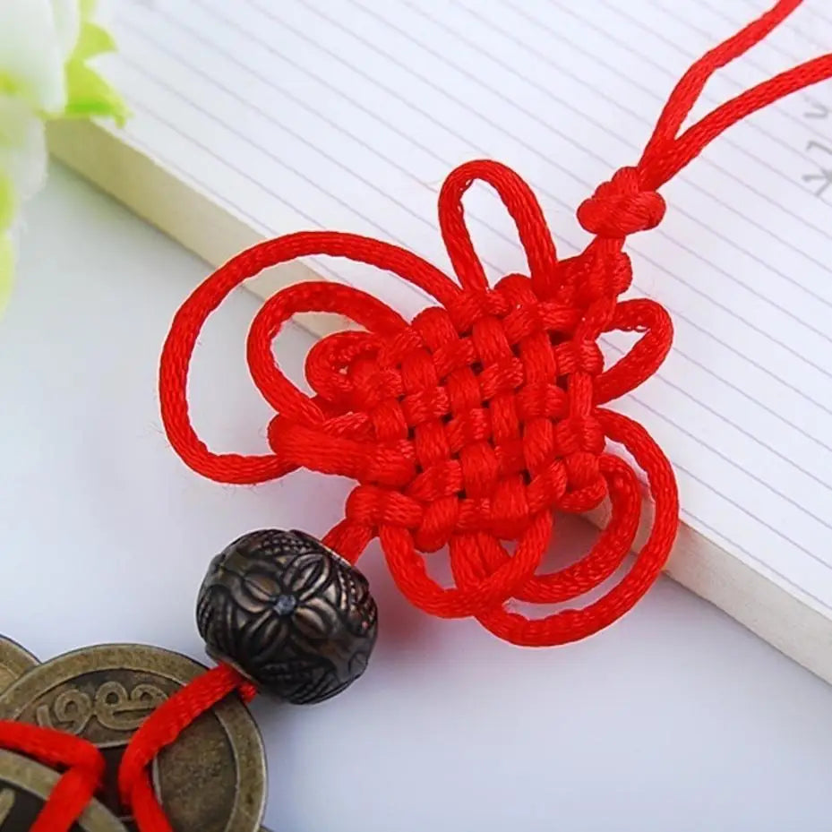 A bright red knotted cord decoration with a dark bead attached, displayed on a white lined paper.