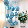 A cluster of ten round blue foil balloons with silver ribbon are suspended against a white wall.