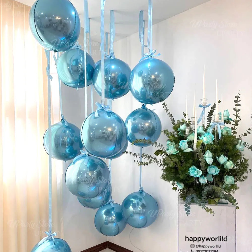 A cluster of ten round blue foil balloons with silver ribbon are suspended against a white wall.