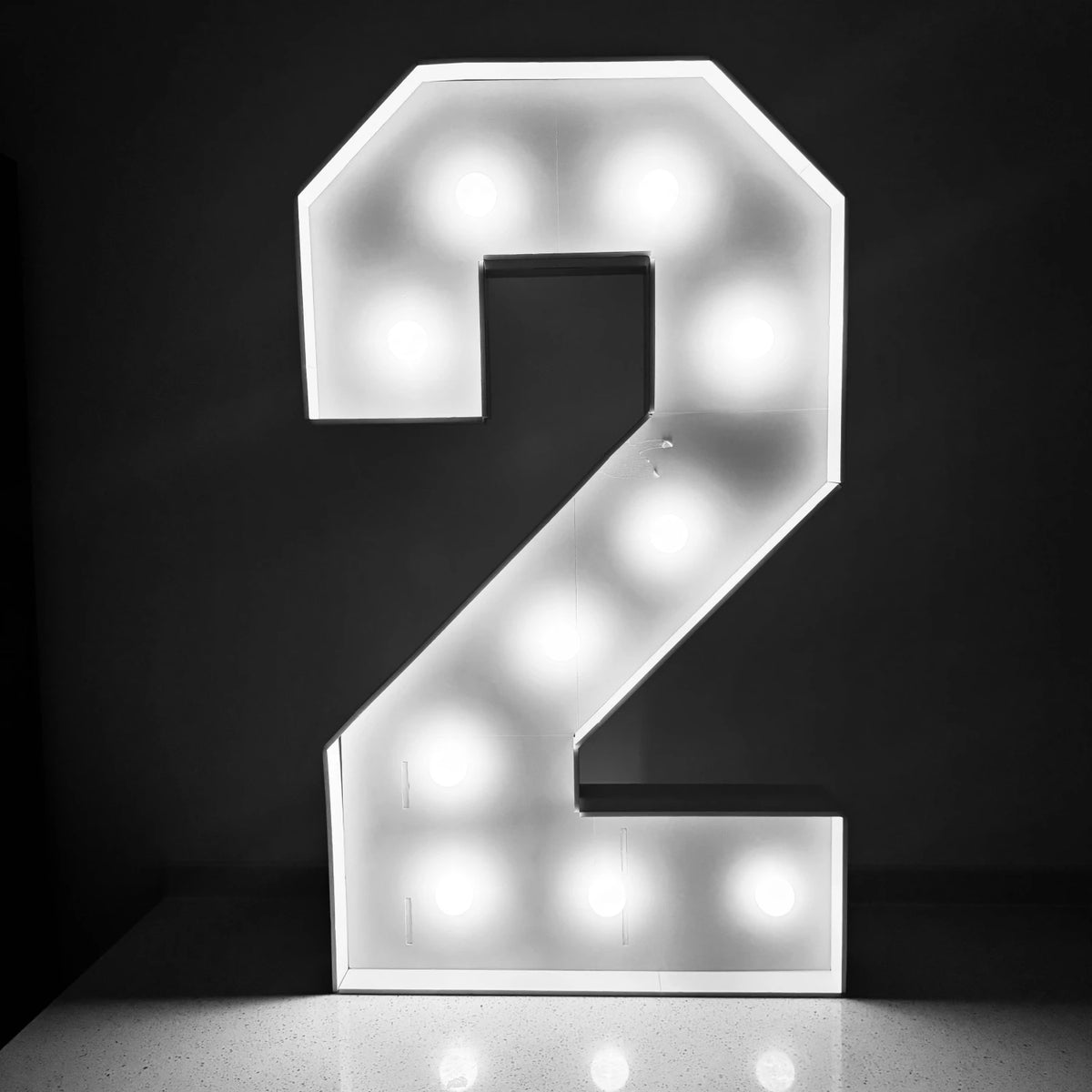 A glowing white marquee number sign shaped like the numeral 2 displayed against a dark background.