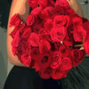 Eine Frau hält einen großen Strauß roter Rosen vor einem dunklen Hintergrund.