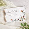 A white personalized wedding guest book with gold binding and delicate floral watercolor accents on a cream linen background.