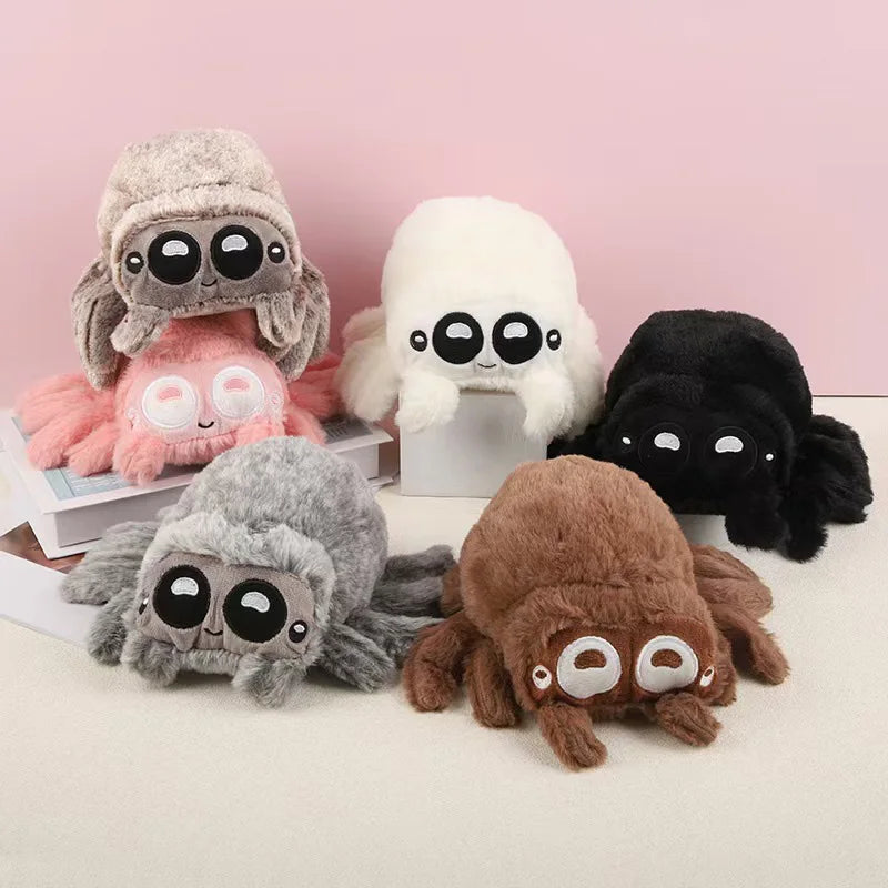 A collection of various plush spider toys in shades of gray, pink, white, and black against a light background.