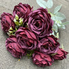 A bouquet of nine deep purple silk roses with green leaves arranged on a gray fabric.