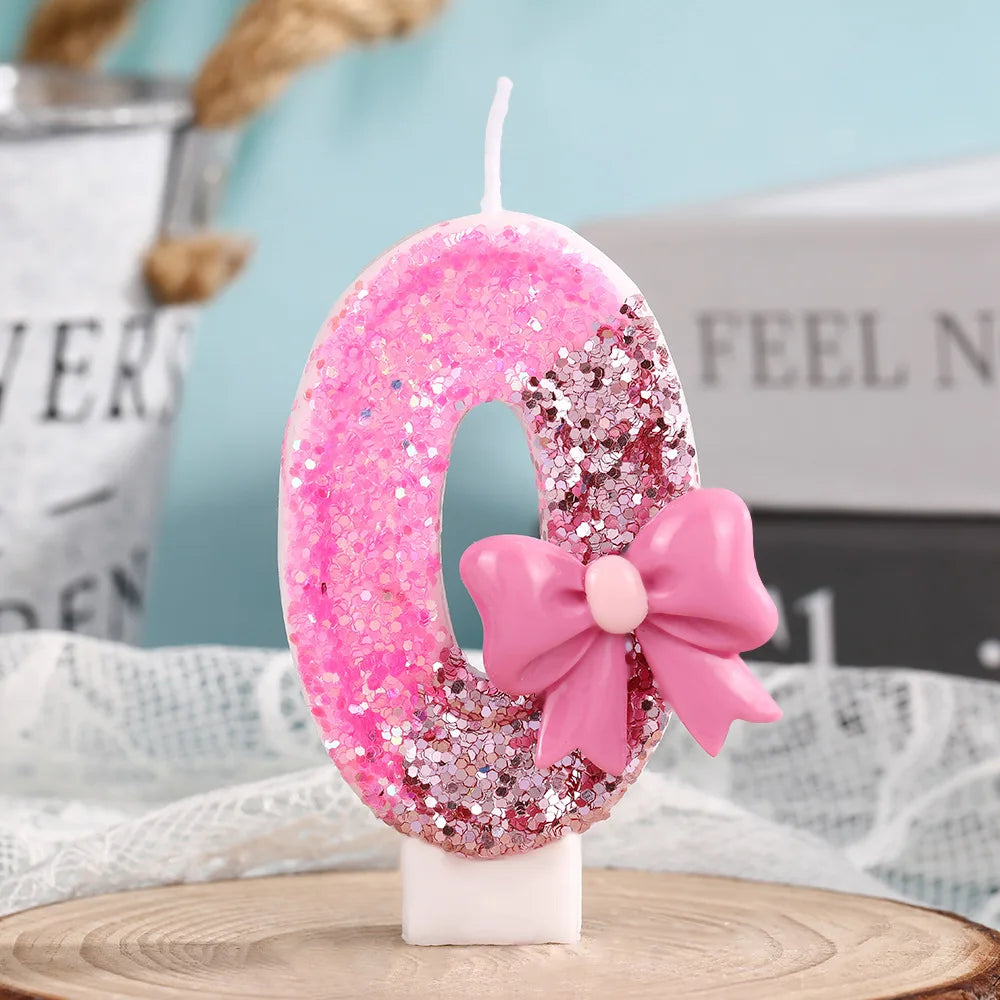 A pink glitter number zero candle with a pink bow on a white stand.