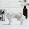 A white plaster bust miniature of a classical Greek figure, displayed on a white surface.