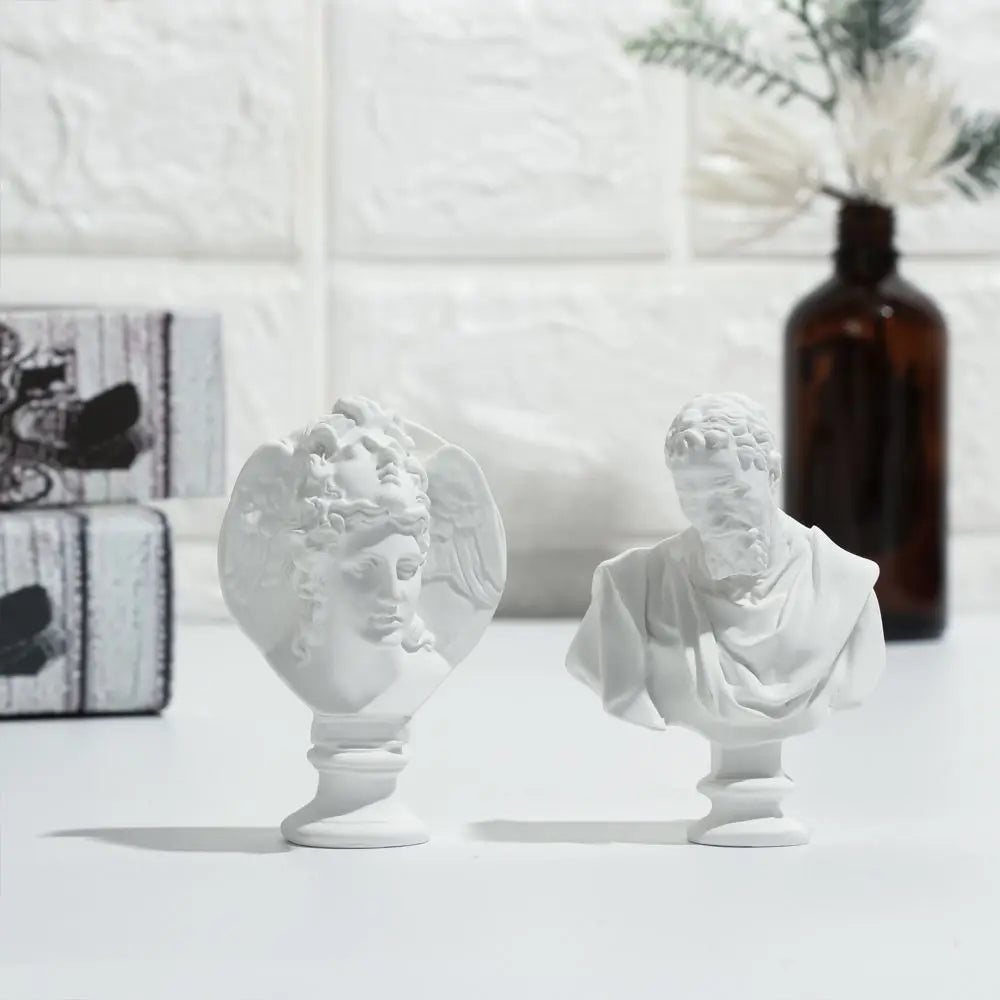 A white plaster bust miniature of a classical Greek figure, displayed on a white surface.